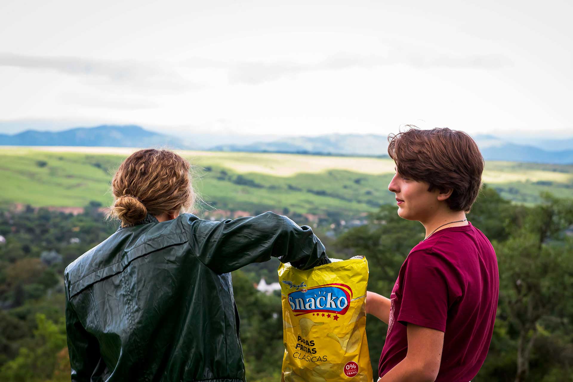 Fotografía de dos adolescentes, en la montaña, compartiendo un paquete de snacks. Campaña para la compañía 'Snacko'