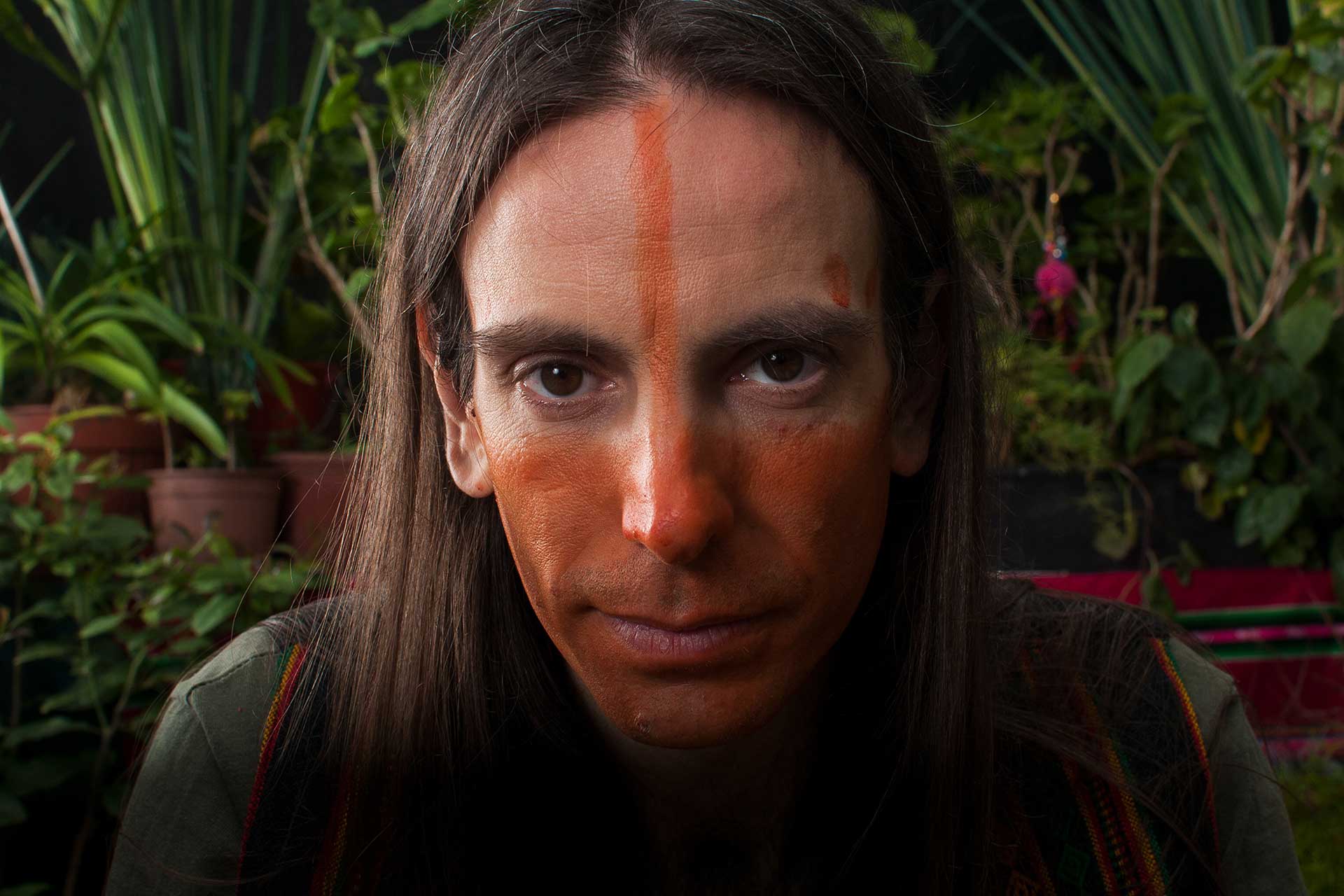Retrato fotográfico de un hombre con la totalidad de su rostro maquillado con un pigmento natural de color rojo
